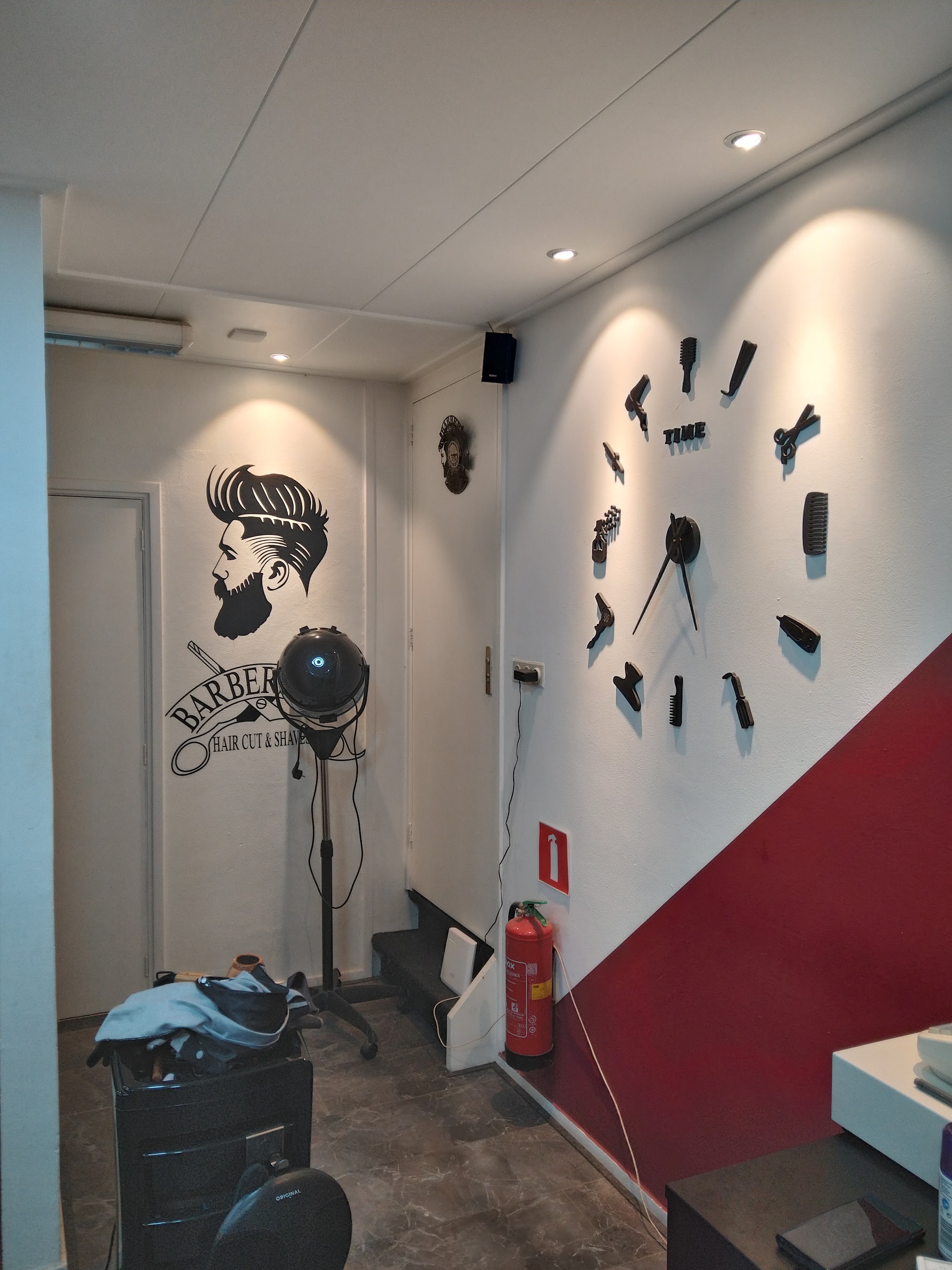 De muur met een grote klok en een bordeaux baan in Kapsalon Oscar